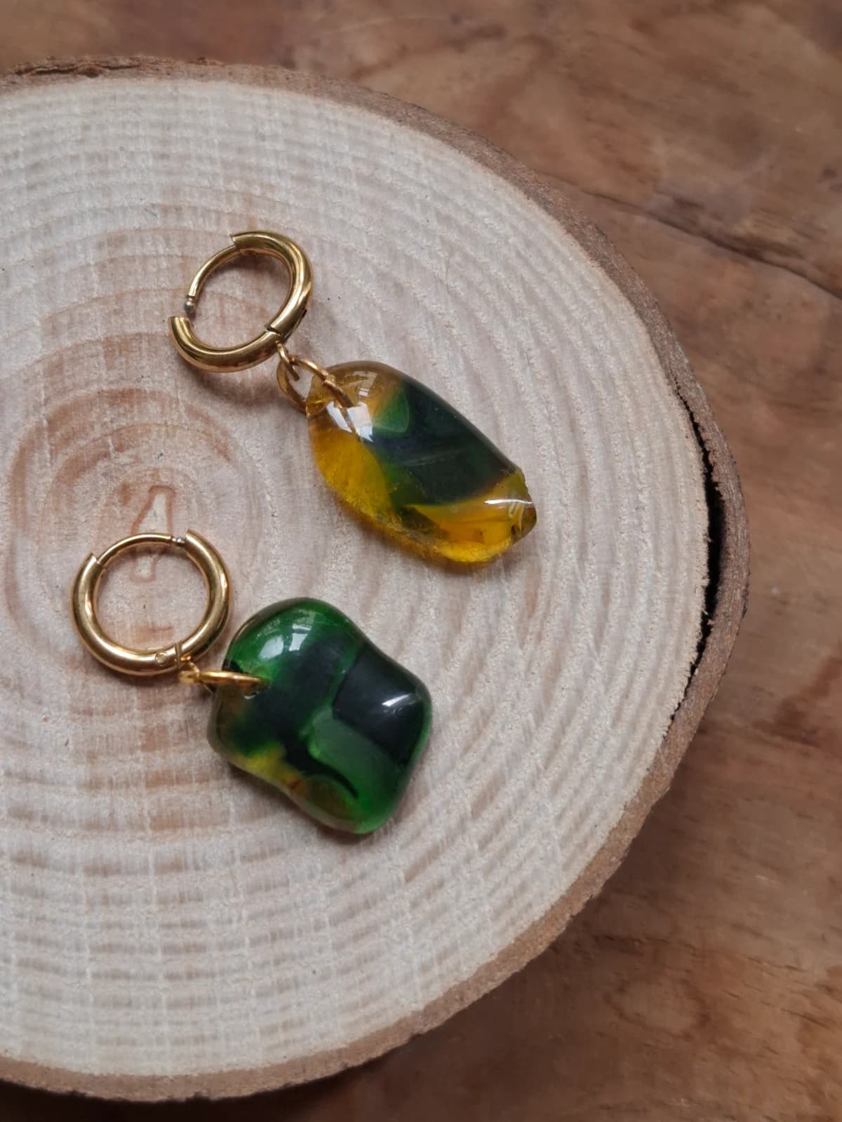 Paire de boucles d'oreilles dorées avec pendentifs en verre vert et jaune posée sur un rondin de bois.
