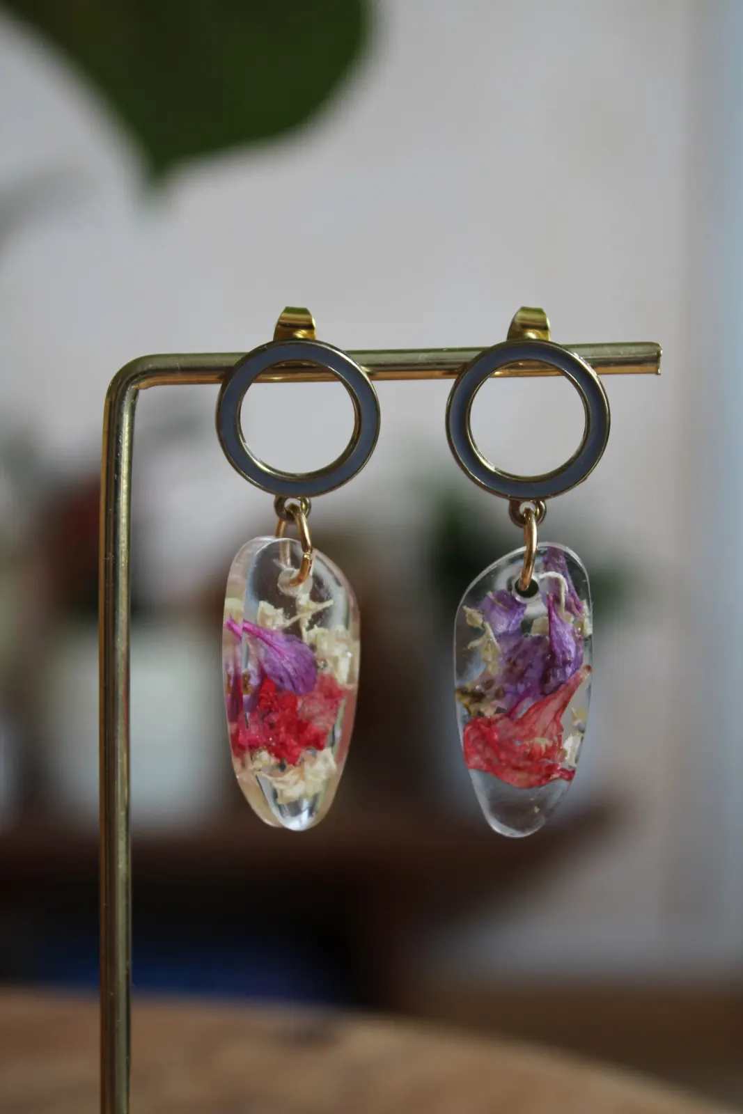 Boucles d'oreilles pendantes en résine transparente avec inclusions florales colorées sur un présentoir.