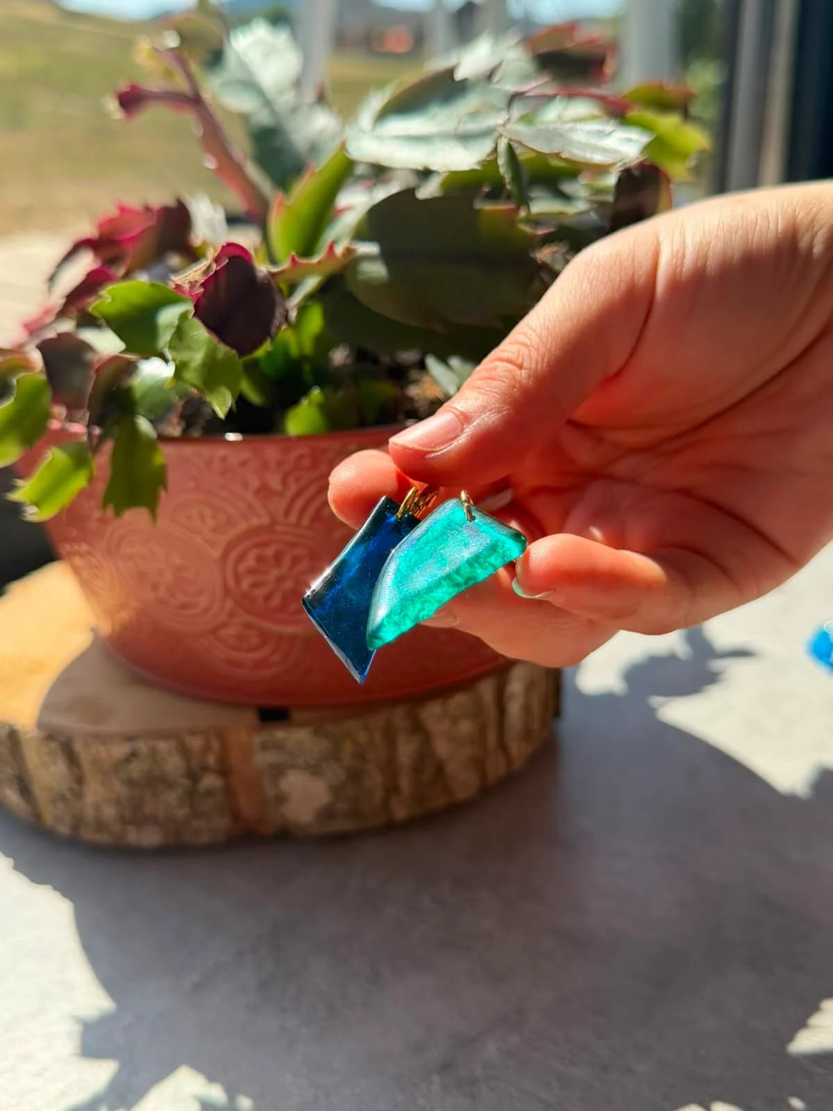 Boucles d'oreilles pendantes asymétriques en verre bleu turquoise et bleu roi tenues en main à la lumière.
