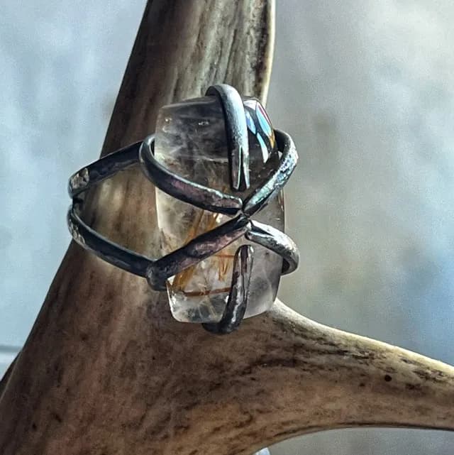 Gros plan sur la bague Sarcophage en argent enserrant un quartz rutile translucide sur un support en bois de cerf.